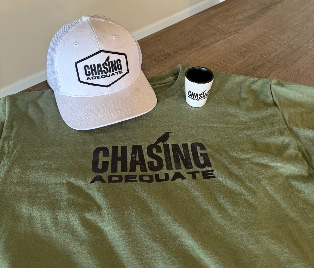 Chasing Adequate merch lineup: trucker hat, t-shirt, and shot glass